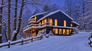 A two-story house with a balcony, surrounded by snow-covered trees.