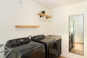 A laundry room with a front-loading washer and dryer, wooden shelves, and a mirror reflecting the door. - Stunning Luxury Retreat With Sweeping Mountain Views!  Something for Everyone! (Gatlinburg)