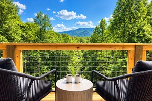 A deck with two chairs and a table, overlooking a forested mountain landscape.