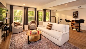 Una sala de estar moderna con un sofá blanco, dos sillones, una mesita con aperitivos y un elemento decorativo en la pared.