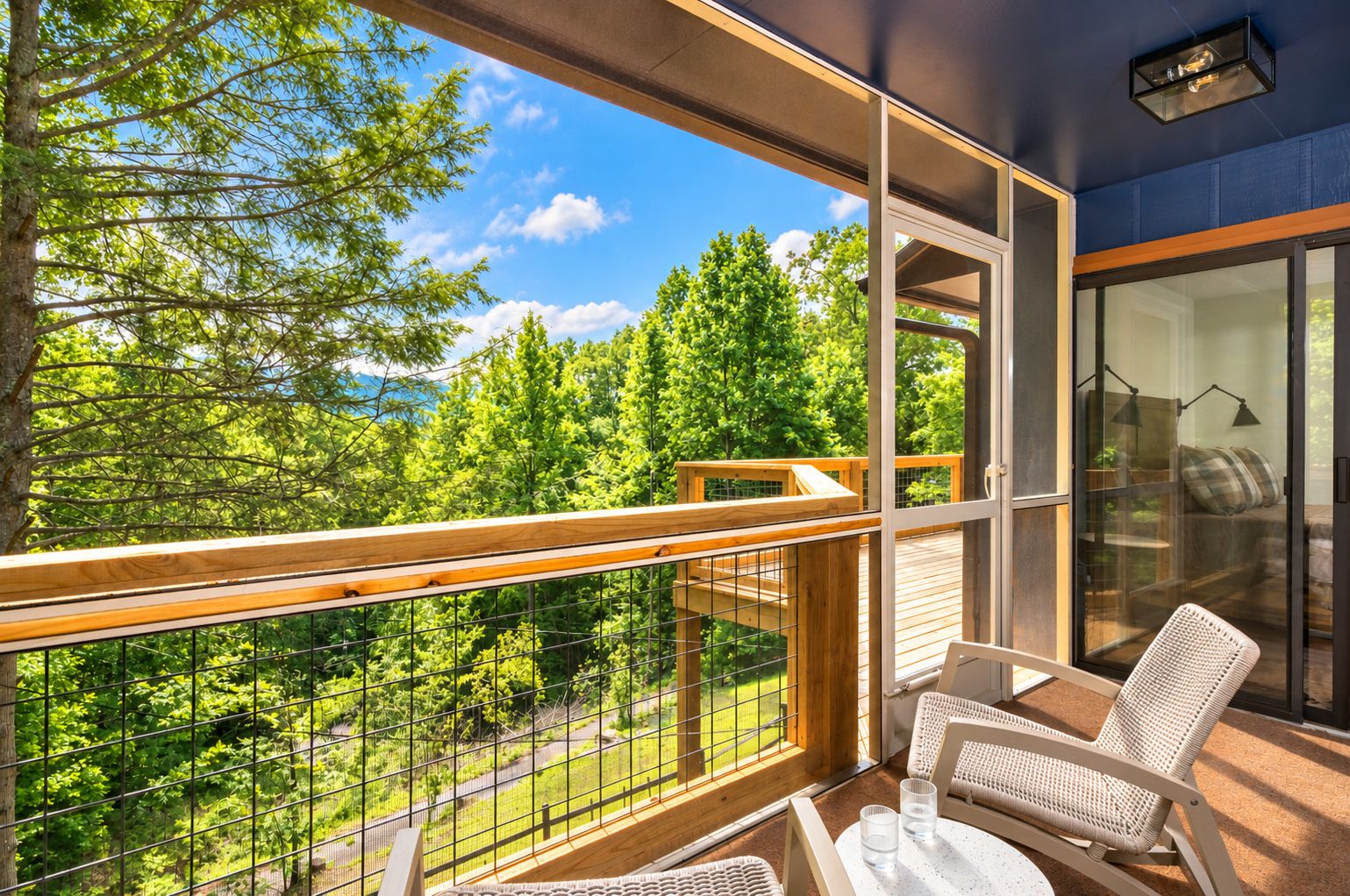 Varanda com vista para uma floresta, porta de vidro que dá para um quarto com sofá e mesa.