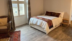 Ein Schlafzimmer mit Bett, Stuhl, Nachttisch und einem fenster mit Vorhängen.