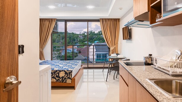 Une chambre d’hôtel compacte dotée d’un balcon, d’une kitchenette et d’un lit recouvert d’une couvre-lit à motifs.
