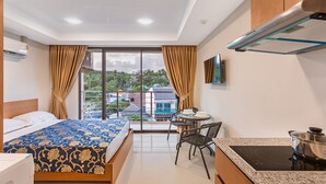 Une chambre d’hôtel comprenant un lit, une table à manger avec des chaises, un coin cuisine et une grande fenêtre avec des rideaux.