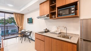 Une cuisine moderne avec des meubles en bois, un évier en acier inoxydable, un four à micro-ondes et une cuisinière. On y trouve également un coin repas avec une table et des chaises, ainsi qu’un balcon offrant une vue sur les maisons.