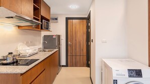 Une cuisine compacte dotée de meubles en bois, d’un four à micro-ondes, d’un réfrigérateur, d’un évier et d’un lave-linge.