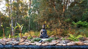 Eine Buddha-Statue in einem Garten mit Teich und dichter Bepflanzung.
