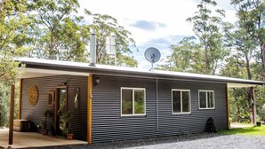 Ein modernes, eingeschossiges Haus mit überdachter Veranda, Satellitenschüssel und Topfpflanzen.