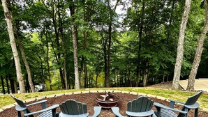 Een ronde zithoek met Adirondack-stoelen rond een vuurkuil, omgeven door bebossing.