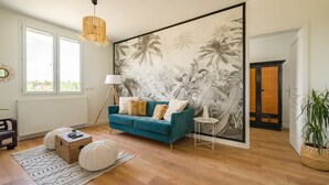 Una sala de estar con un sofá color turquesa, un amplio mural tropical, una lámpara de pie y una planta en maceta.
