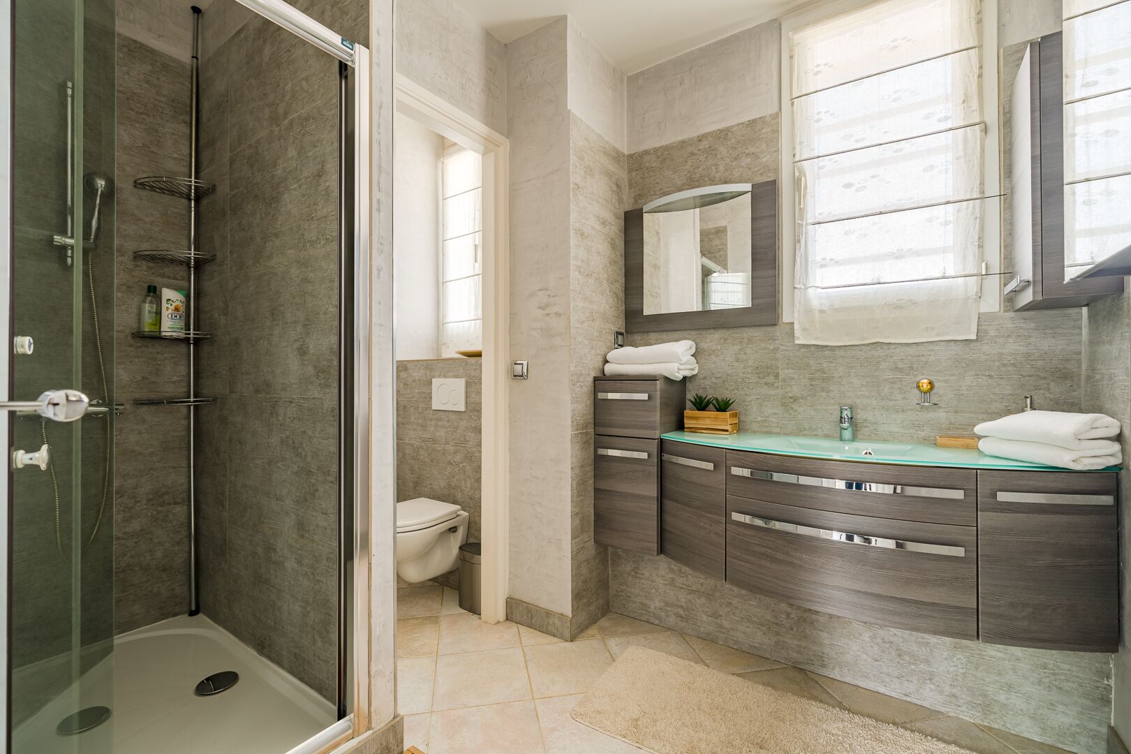 A modern bathroom with a glass-enclosed shower, a toilet, and a vanity with a mirror.