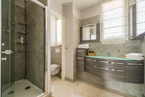 A modern bathroom with a glass-enclosed shower, a toilet, and a vanity with a mirror.
