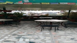 An outdoor patio with tiled flooring, round tables, and chairs, surrounded by potted plants. - MeroStay 192 Home HTS (Kathmandu)