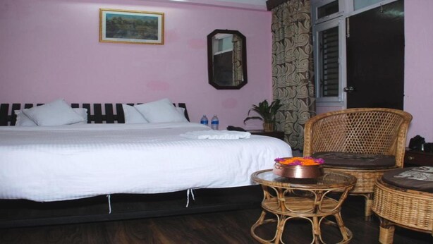 A bedroom with a large bed, a small round table with a flower vase, and two wicker chairs. - MeroStay 192 Home HTS (Kathmandu)