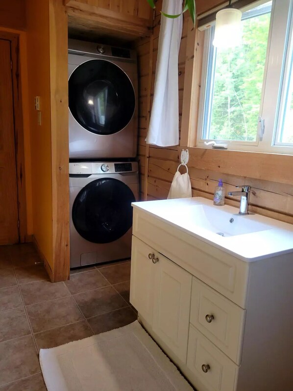 A compact bathroom with a washing machine, a sink with a mirror, and a window.