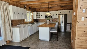 Une cuisine moderne avec des meubles blancs, un îlot central en bois, des appareils électroménagers en acier inoxydable et un sol carrelé de couleur noire.