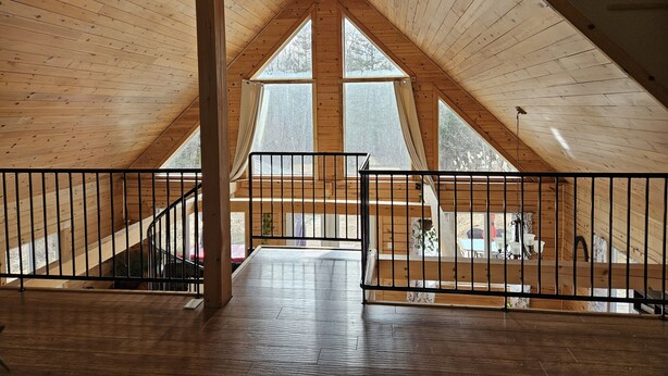 Une pièce mansardée spacieuse avec des poutres en bois, de grandes fenêtres et un ventilateur de plafond.