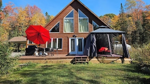 Une cabane en bois avec une terrasse, un parasol rouge et un espace salon extérieur abrité.