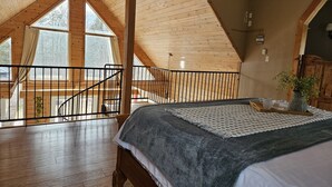 Une chambre avec un grand lit, un plafond en bois et une vue sur l’extérieur par une fenêtre.