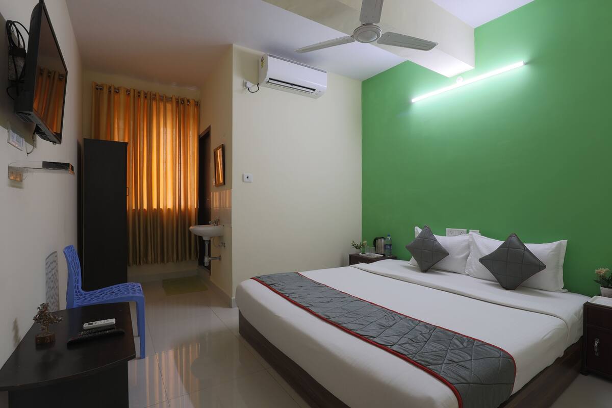 Habitación de hotel con cama, escritorio, silla, televisor, aire acondicionado y ventilador de techo.