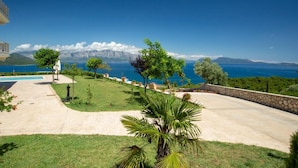 A landscaped garden with a pool, a stone wall, and a view of the sea and mountains. - Villa Ventalia with magnificent panoramic sea view! (Lefkada)