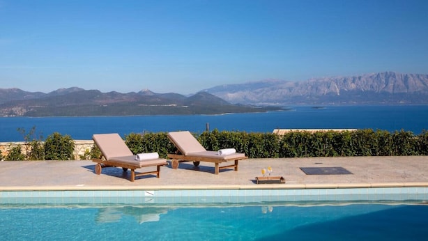 A poolside area with lounge chairs and a view of the sea and mountains. - Villa Ventalia with magnificent panoramic sea view! (Lefkada)