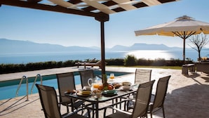 A poolside dining area with a table set for breakfast, overlooking a body of water and mountains. - Villa Ventalia with magnificent panoramic sea view! (Lefkada)