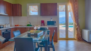A modern kitchen with wooden cabinets, a glass dining table, and a view of the outdoors. - Villa Ventalia with magnificent panoramic sea view! (Lefkada)