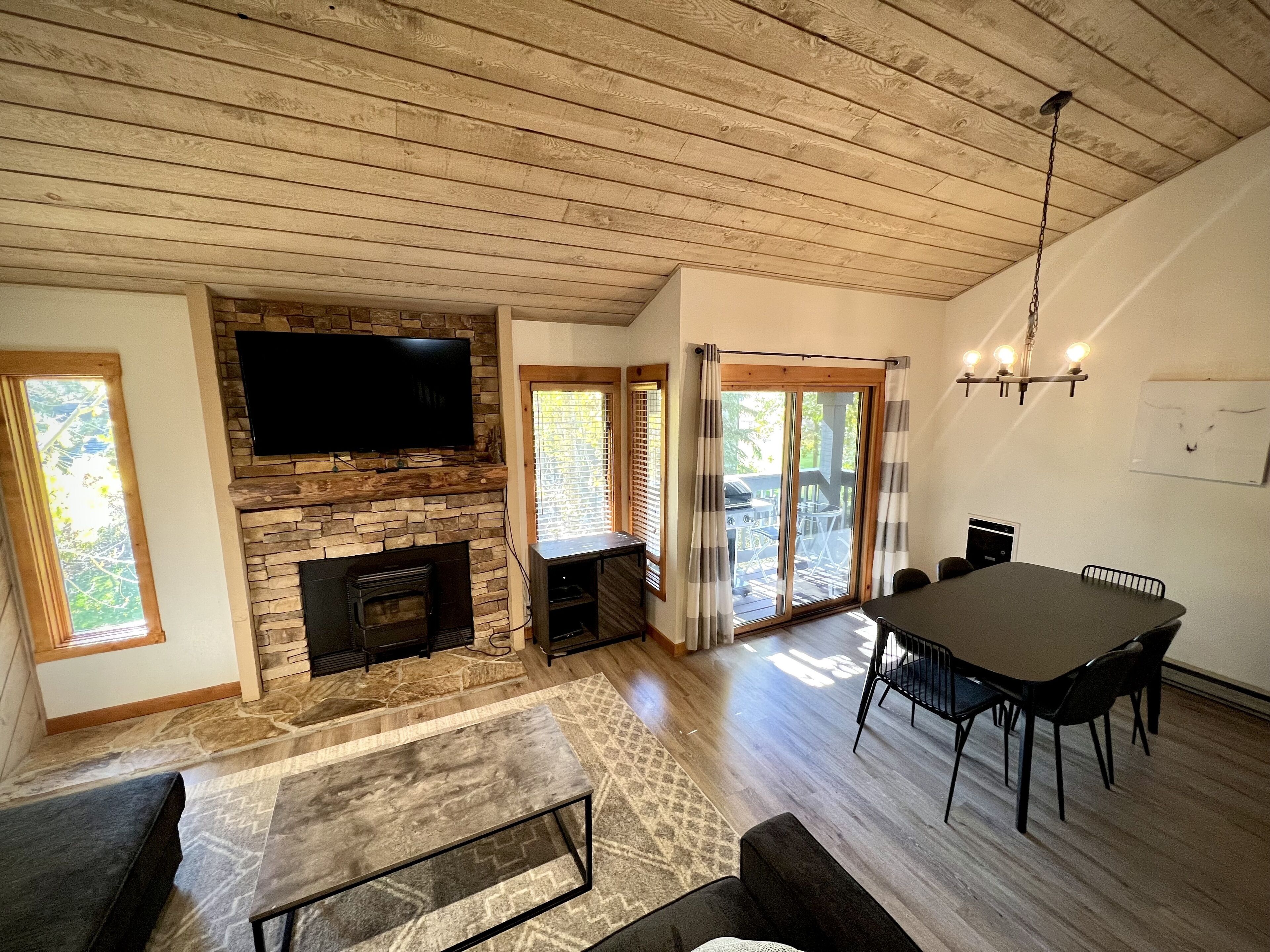 A spacious living area with a stone fireplace, a flat-screen TV mounted above it, and a dining table with chairs.
