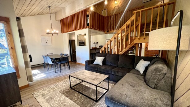 En moderne stue med sofa, sofabord og spiseområde. En trappe fører op til en etage.