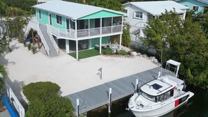 A waterfront property with a boat dock, a covered deck, and a two-story house with a green roof.