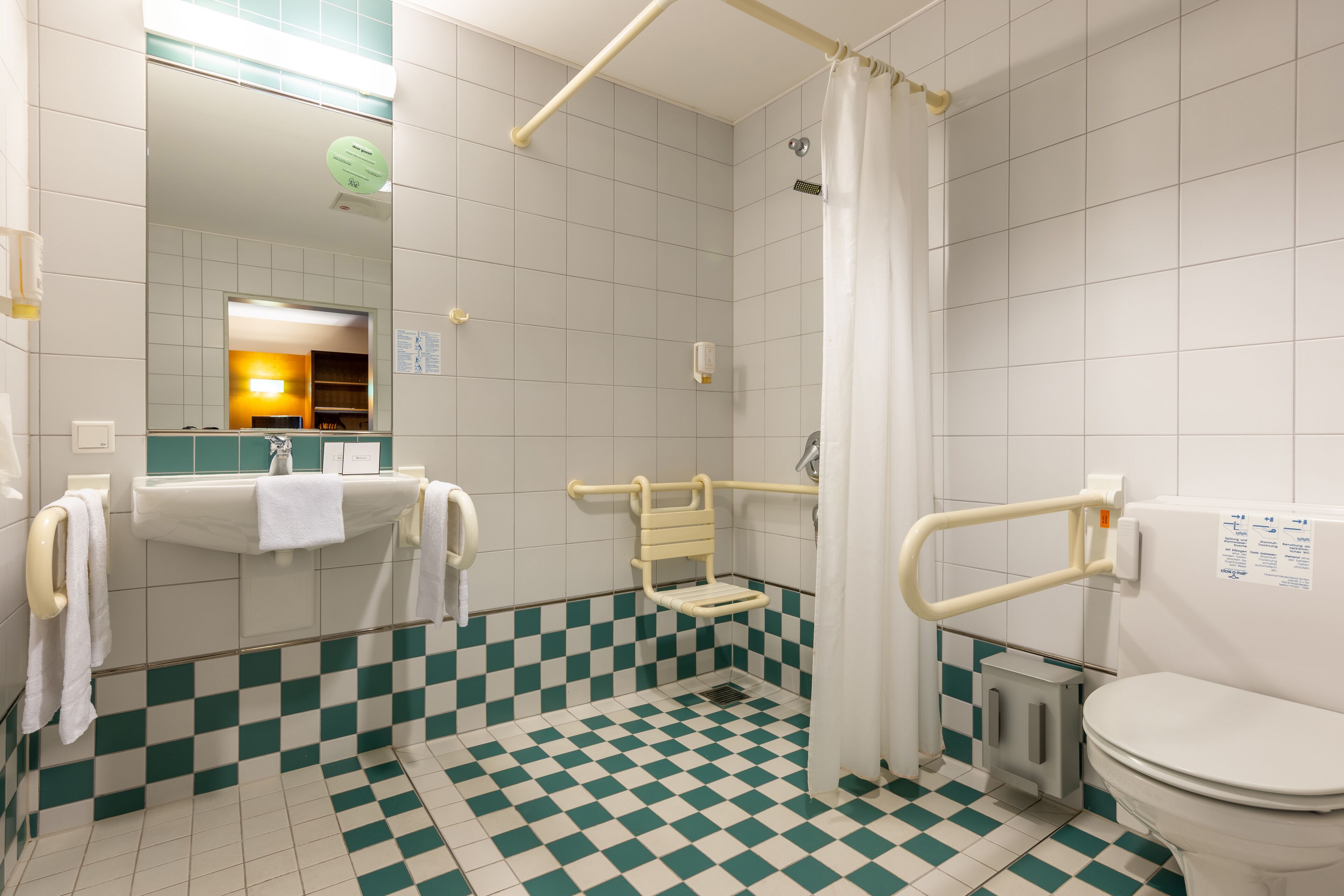 A bathroom with a checkered floor, a toilet, a sink with a towel, and a shower area.