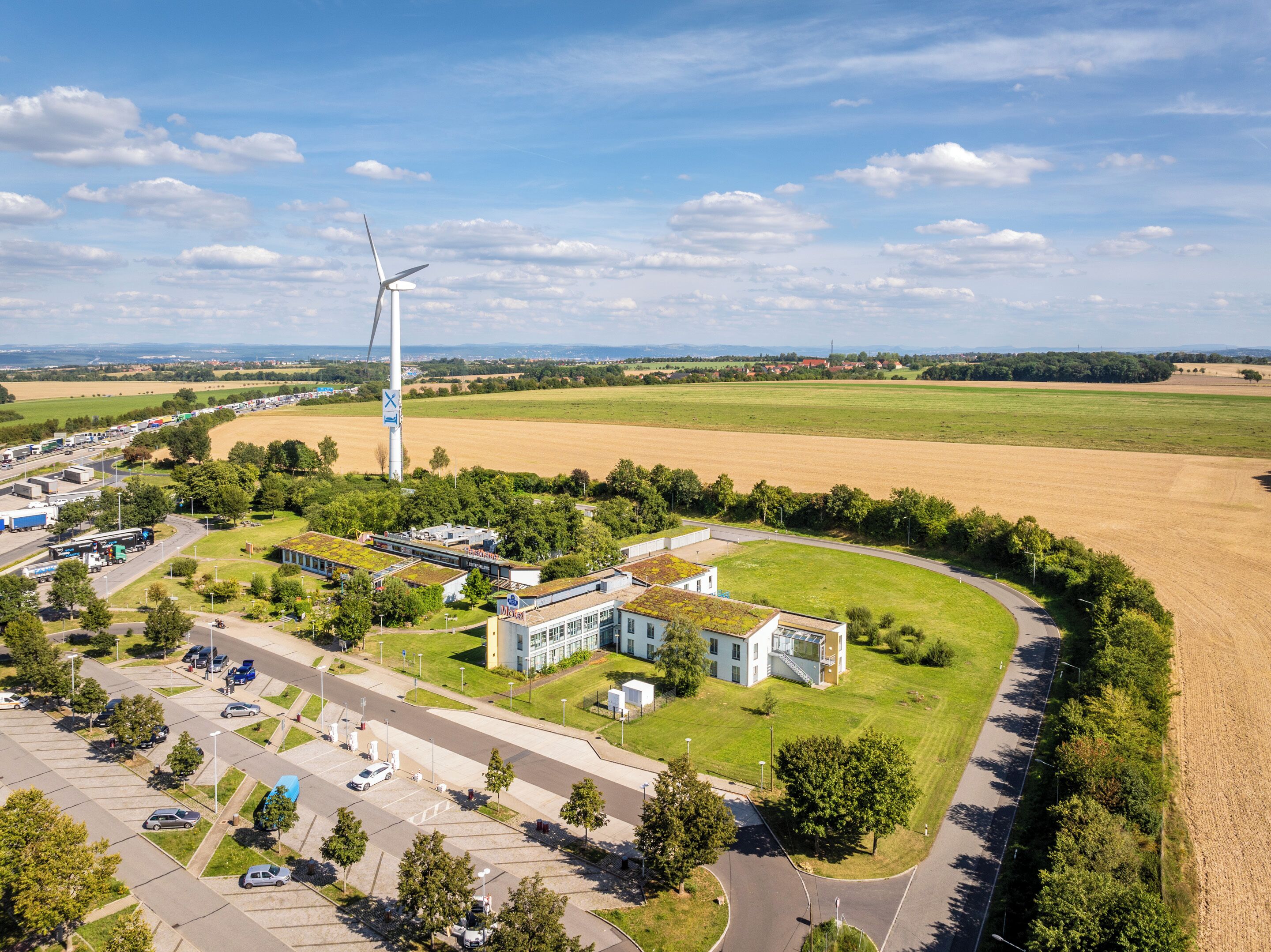 An industrial area with a large wind turbine, modern buildings, and a parking lot.