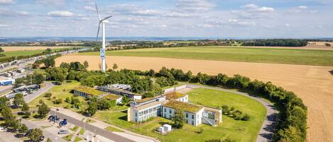 An industrial area with a large wind turbine, modern buildings, and a parking lot.