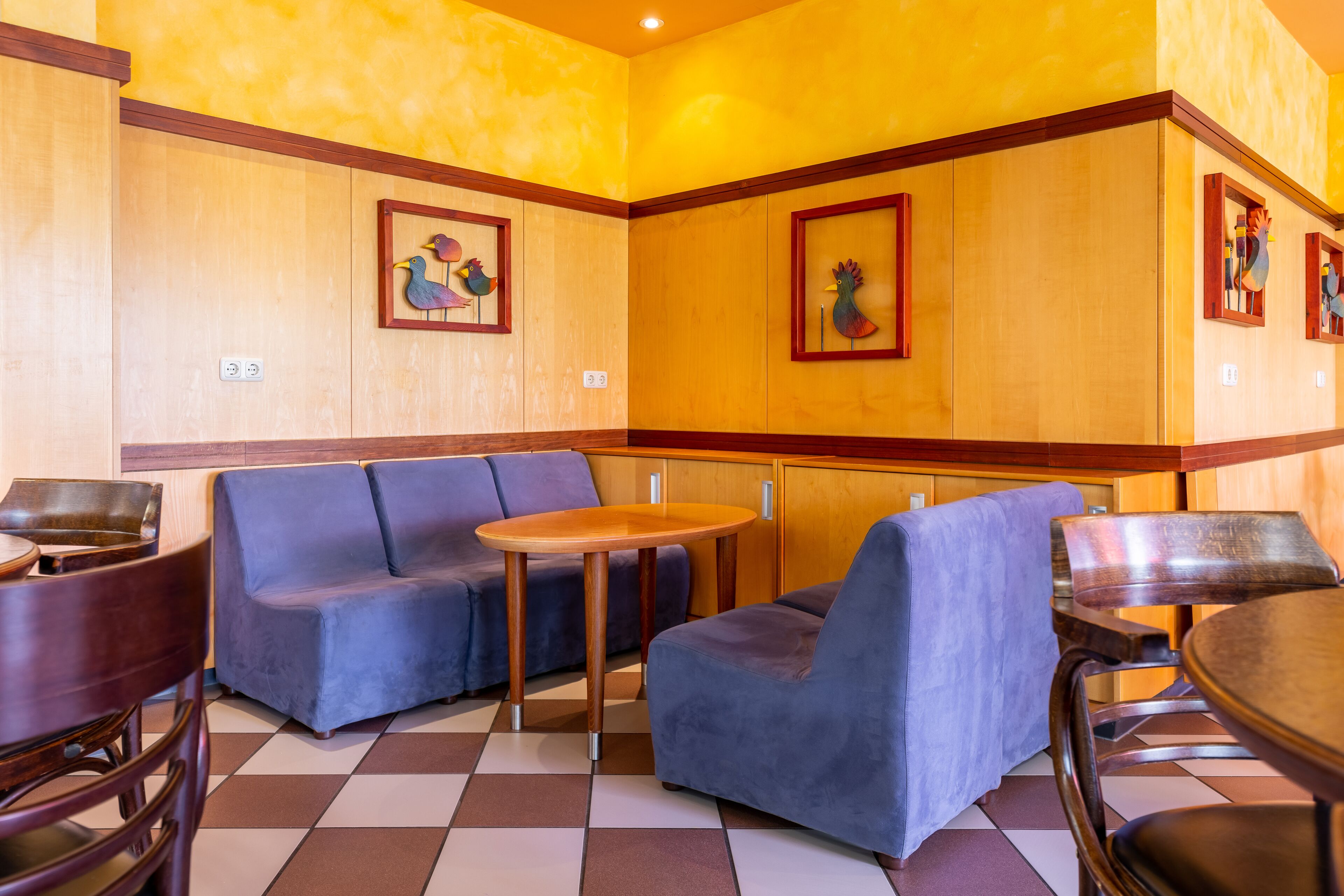 En restaurang med väggar beklädda med träpaneler, blå stoppade sittplatser och ett rutmönstrat golv.