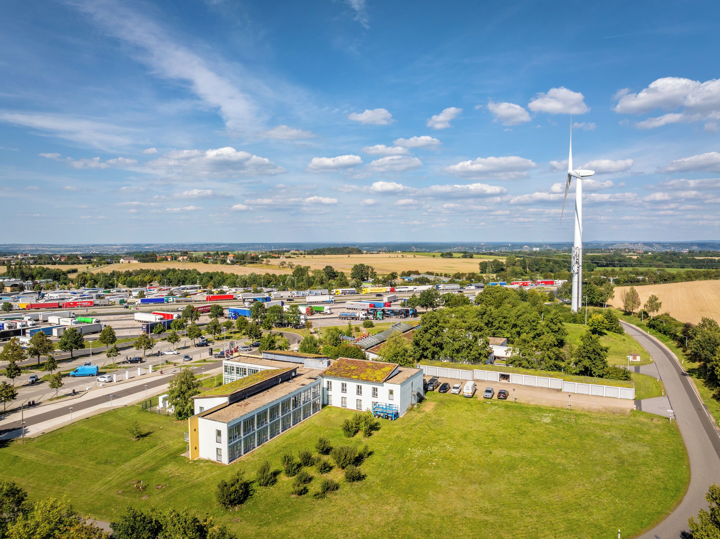 Une zone industrielle comprenant une grande éolienne, un parking et un bâtiment doté d’un toit végétalisé.