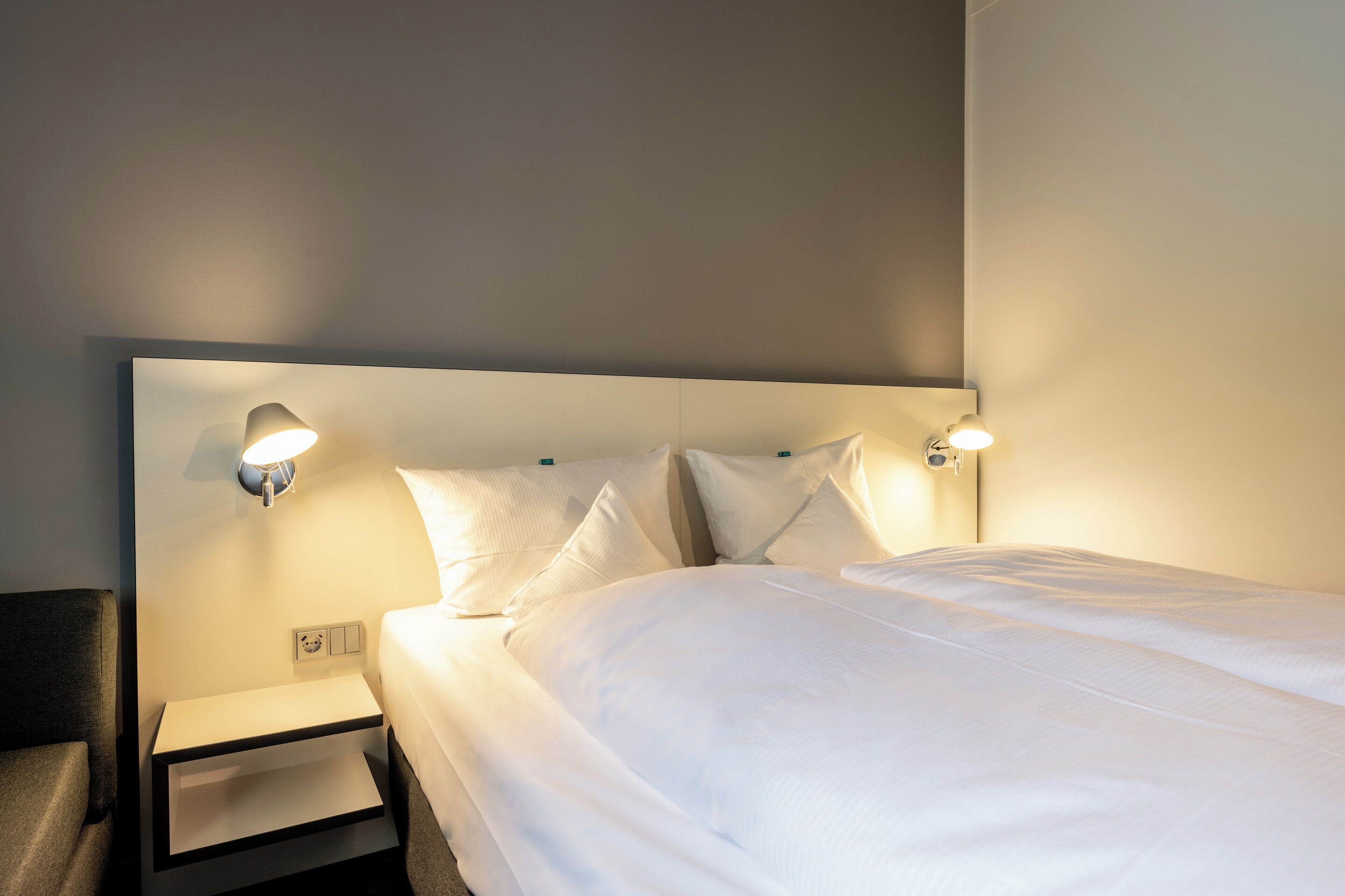 A neatly made bed with white linens, two bedside tables, and wall-mounted reading lamps.