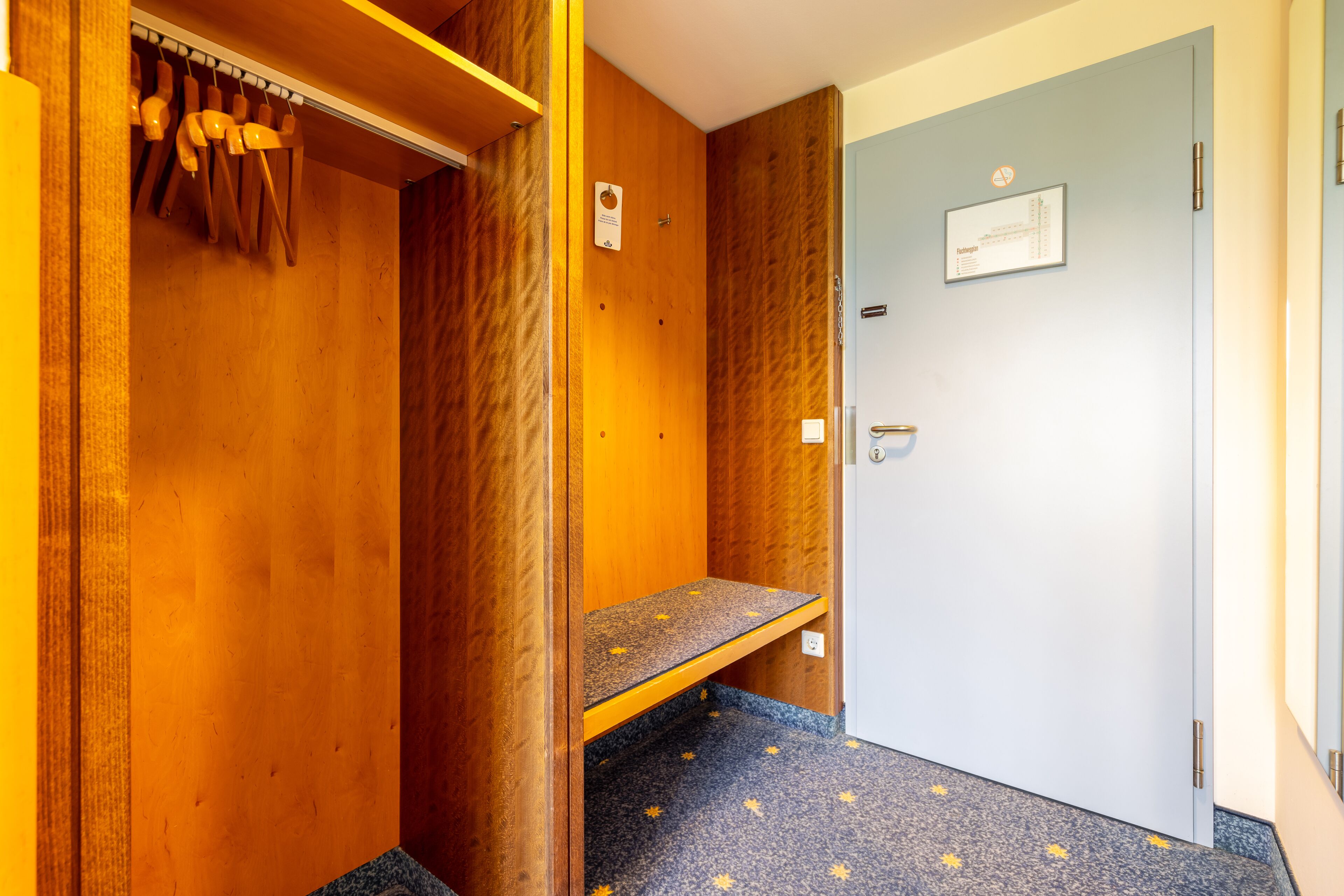 A wooden interior with a bench, a door with a sign, and a coat rack.