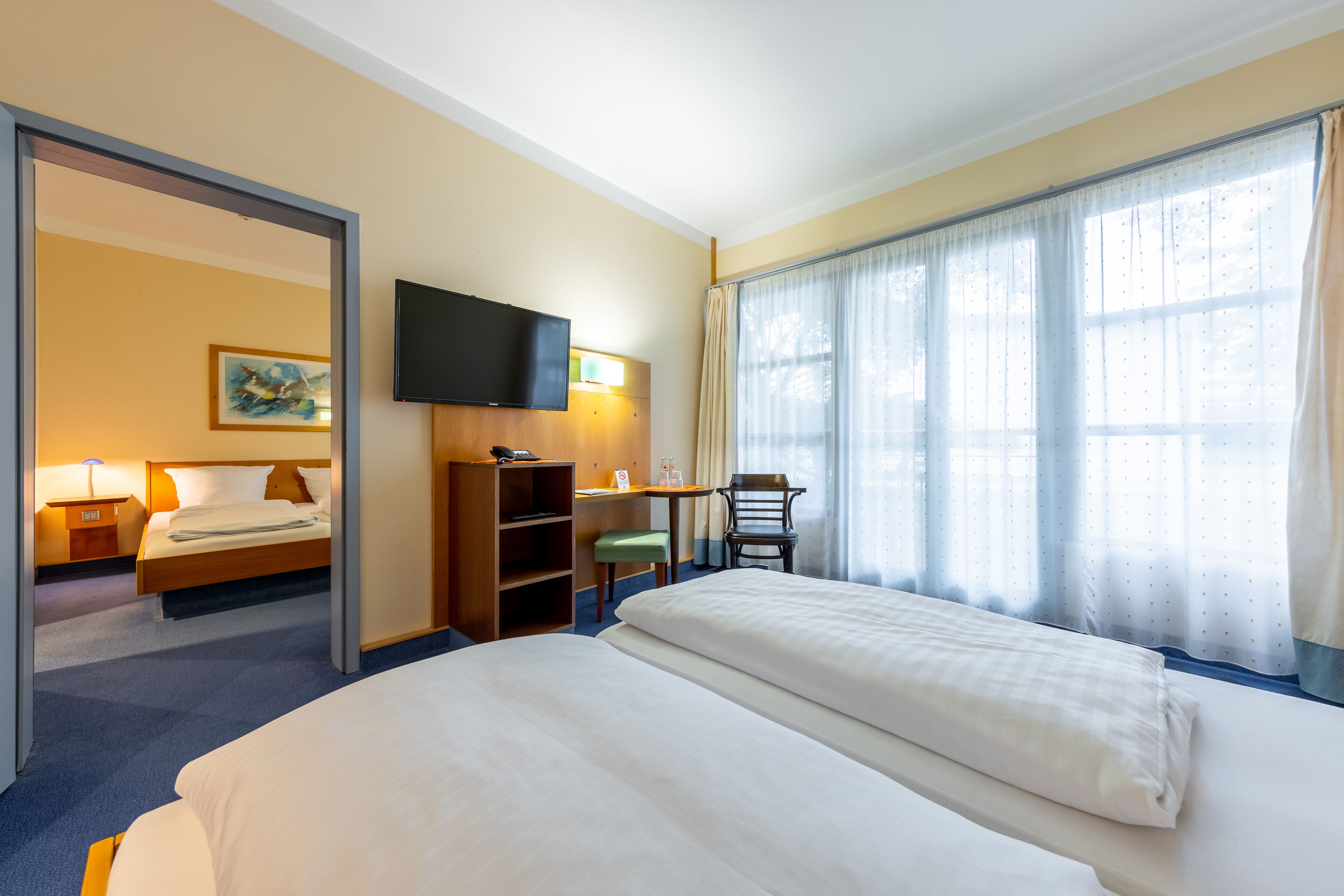 A hotel room with a large bed, a desk with a chair, a television, and a window with curtains.
