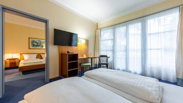 Ein Hotelzimmer mit einem großen Bett, einem Schreibtisch mit Stuhl, einem Fernseher und einem Fenster mit Vorhängen.