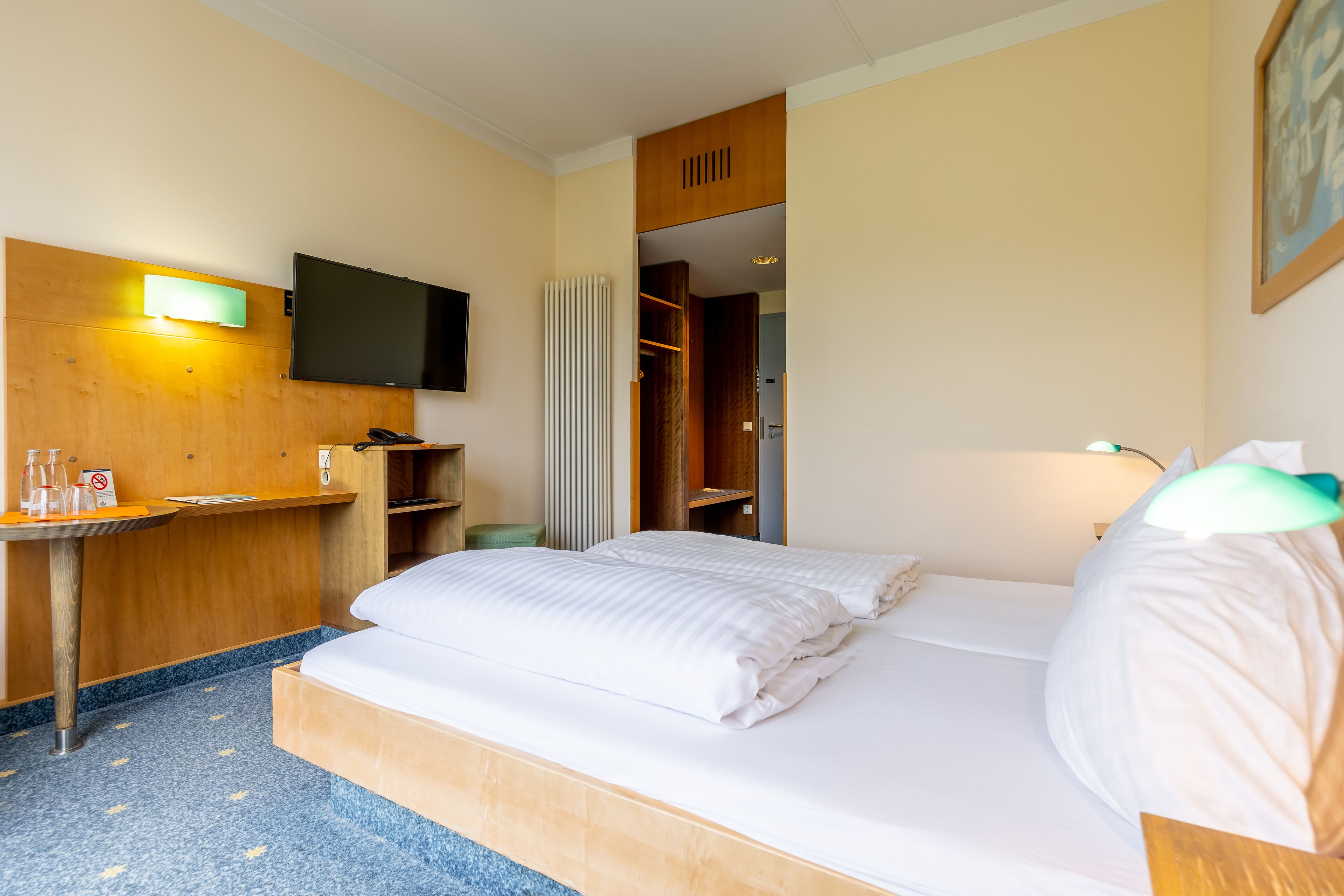 Una habitación de hotel con cama, escritorio, televisor y armario.