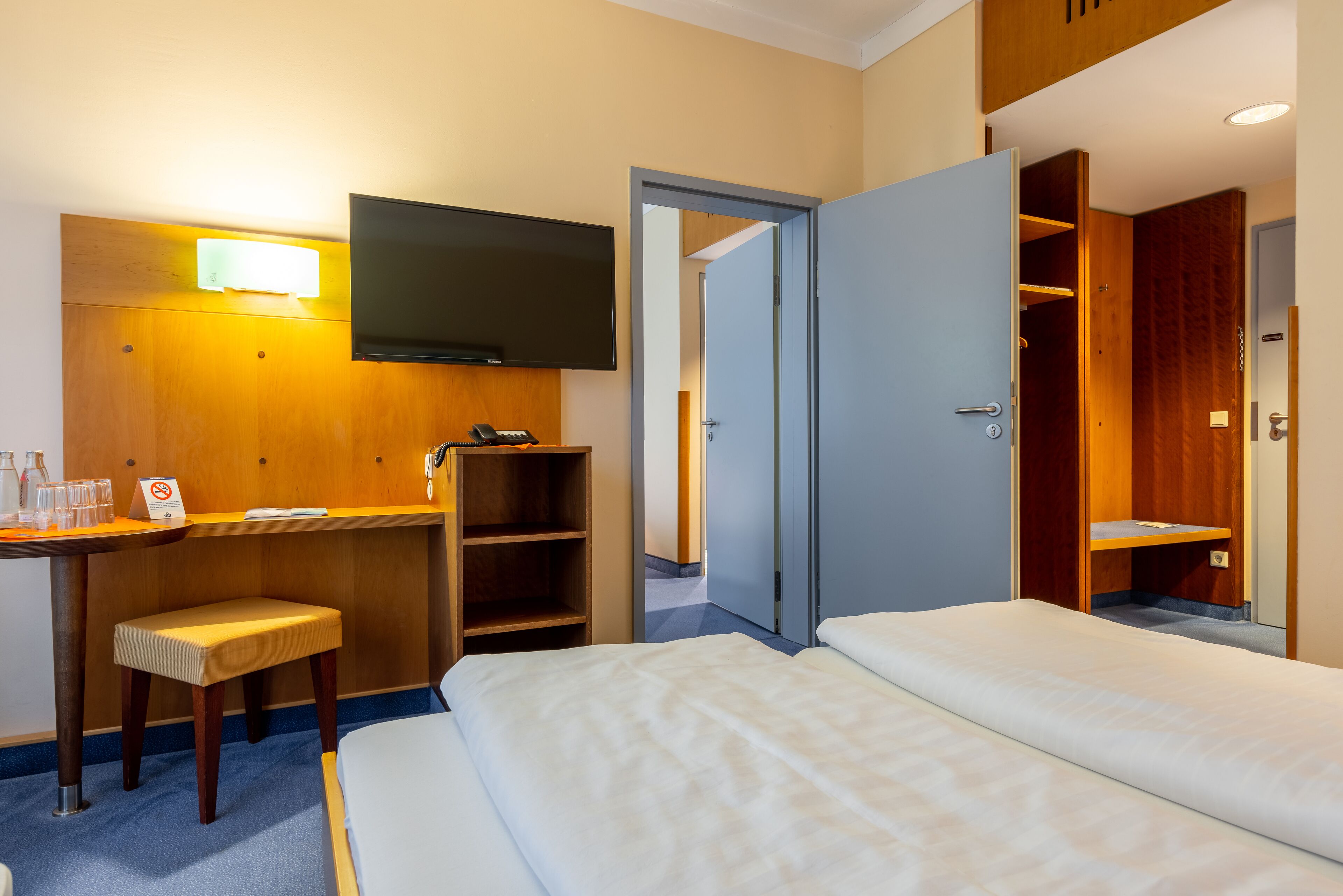 Una habitación de hotel con cama, escritorio con silla, televisor y armario.