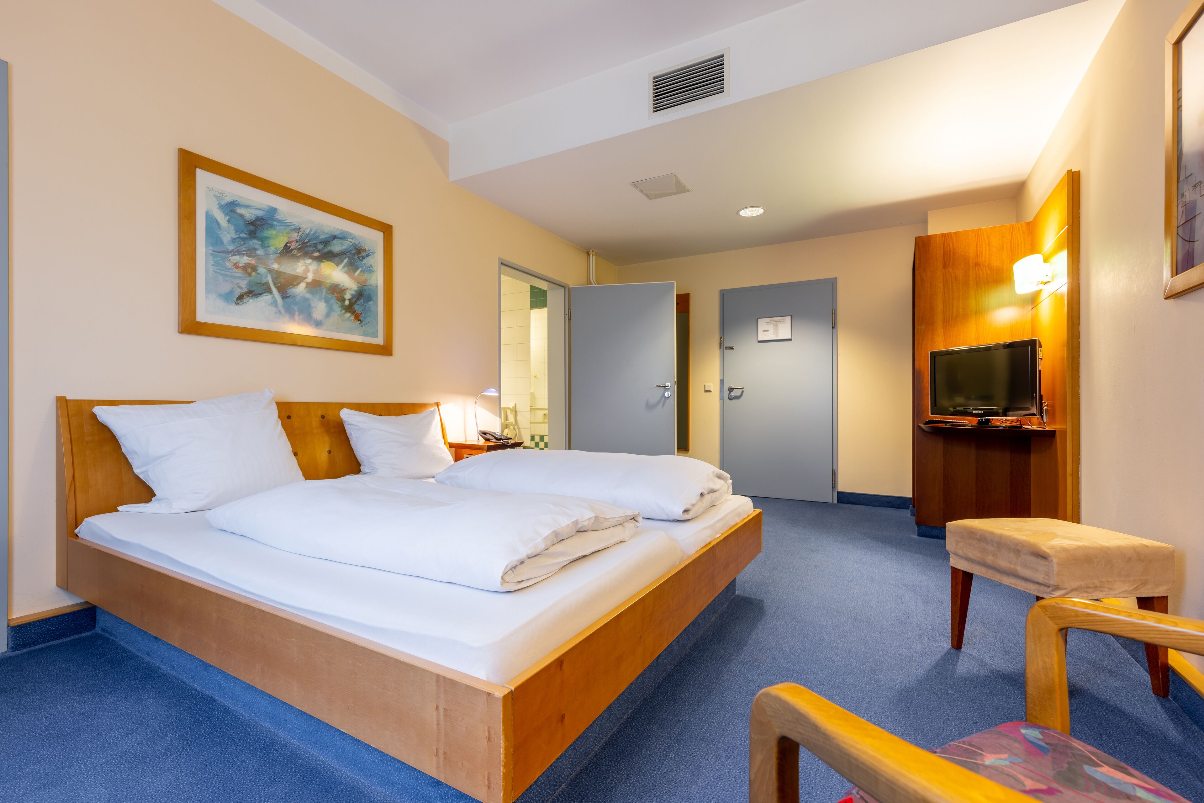 A hotel room with a double bed, a wooden headboard, a TV, a desk, and a chair.