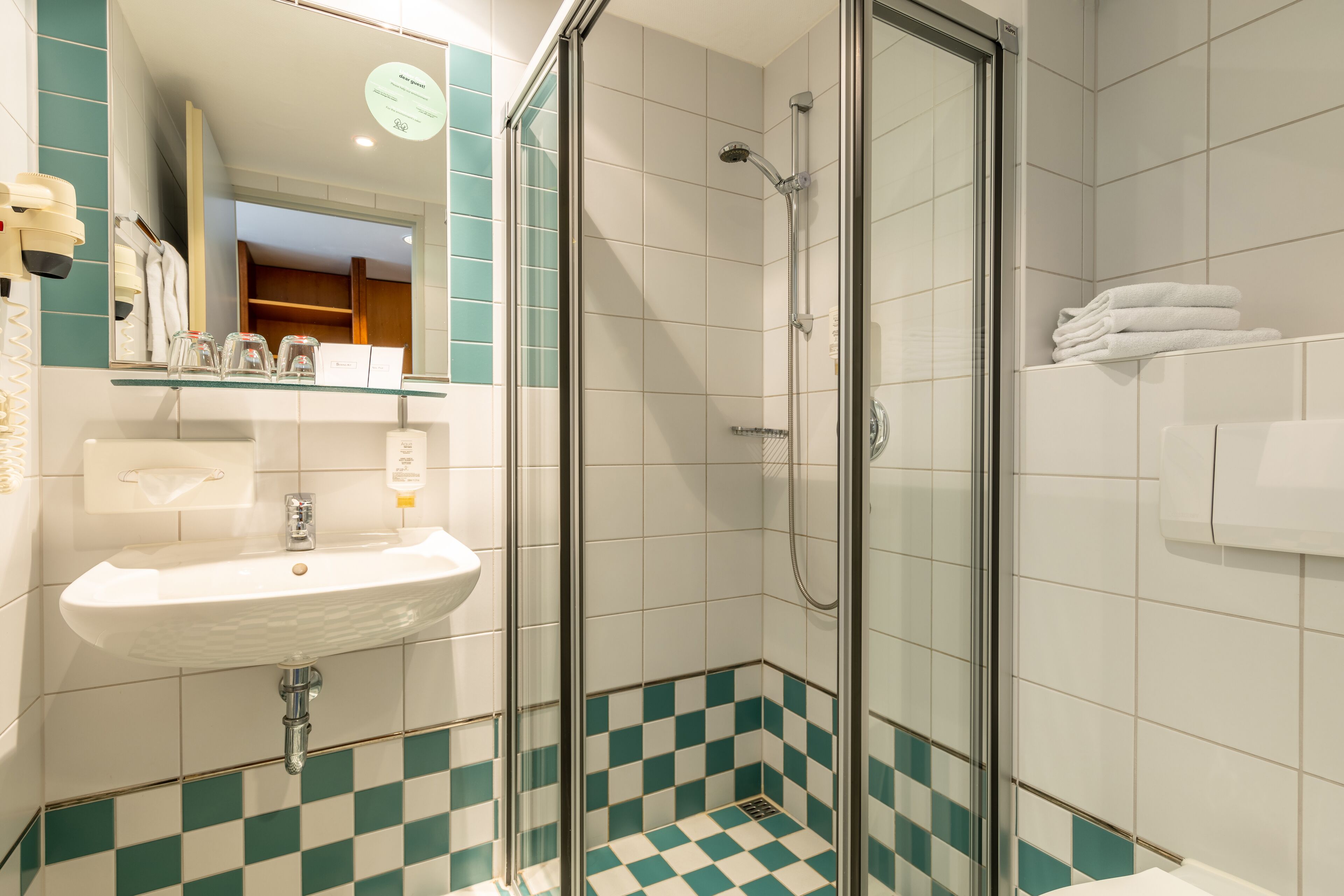 Une salle de bain avec une douche à parois de verre, un lavabo blanc et des carreaux de sol à motifs à carreaux.
