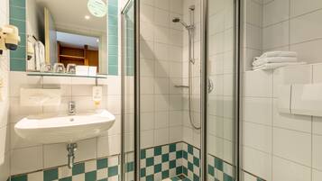 A bathroom with a glass-enclosed shower, a white sink, and checkered floor tiles.