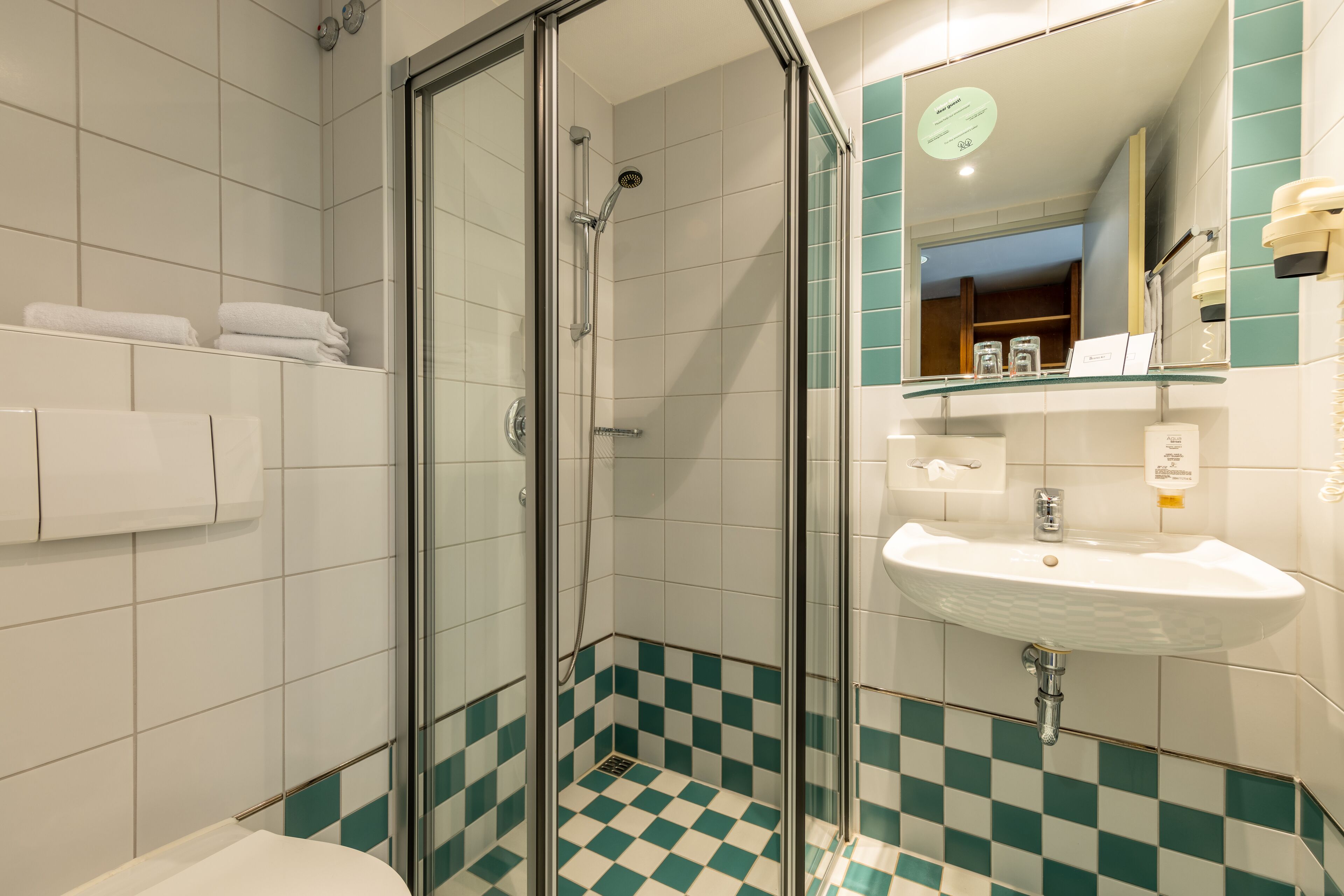 A bathroom with a glass-enclosed shower, a sink, and checkered floor tiles.