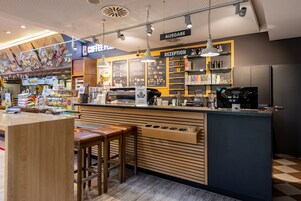 A modern coffee shop interior with a reception area, wooden counter, and bar stools.