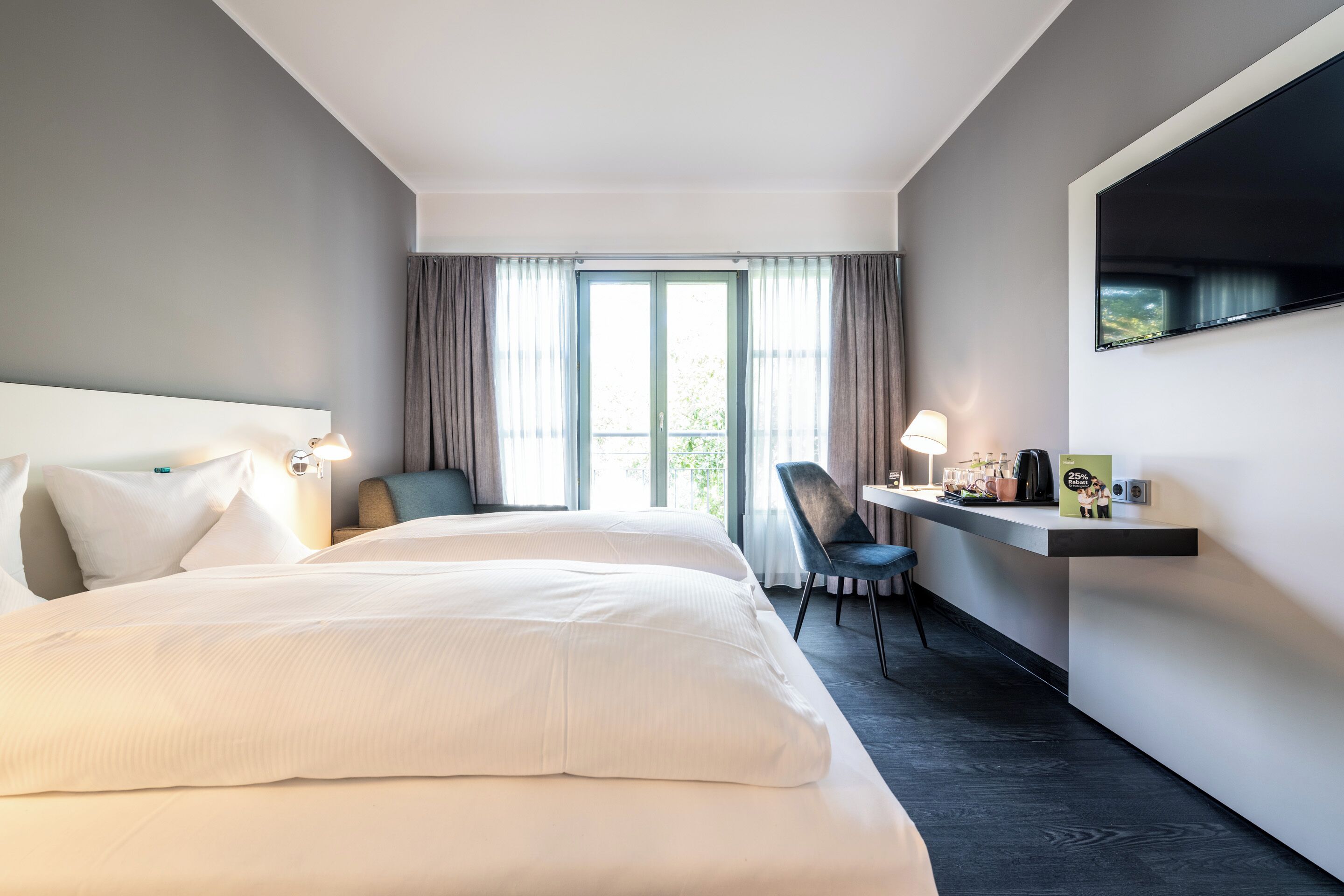 Habitación de hotel con una cama grande, un escritorio con silla, televisión y ventana con cortinas.