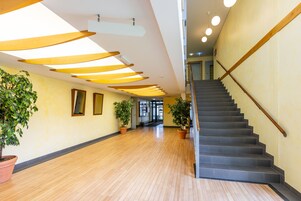 A spacious hallway with wooden flooring, potted plants, and a staircase with a wooden handrail.