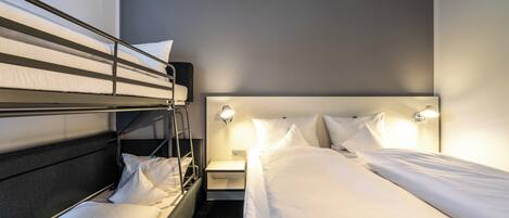 A hotel room with a bunk bed, a single bed, a nightstand with a lamp, and a wall-mounted light fixture.